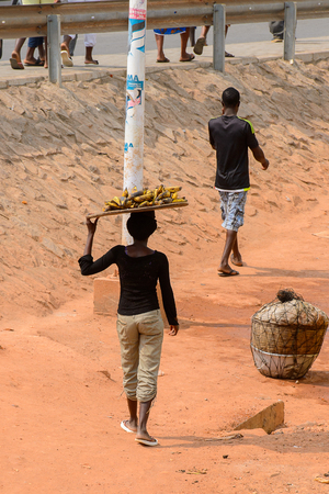 ELMINA, GHANA -JAN 18, 2017: Unidentified  Ghanaian woman carries a tray with bananas on her head in Elmina. People of Ghana suffer of poverty due to the bad economyのeditorial素材