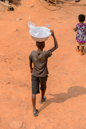 ELMINA, GHANA -JAN 18, 2017: Unidentified  Ghanaian boy carries a basin on his head in Elmina. Children of Ghana suffer of poverty due to the bad economyのeditorial素材