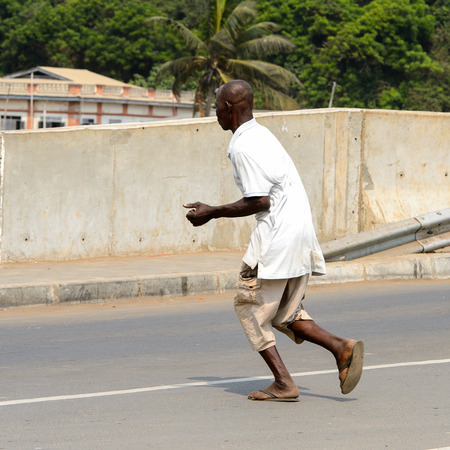 ELMINA, GHANA -JAN 18, 2017: Unidentified  Ghanaian man runs across the road in Elmina. People of Ghana suffer of poverty due to the bad economyのeditorial素材