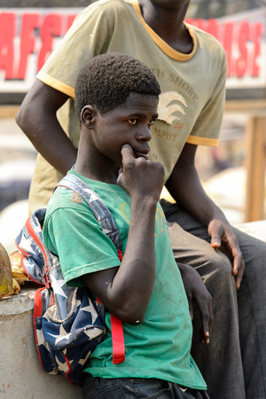 ELMINA, GHANA -JAN 18, 2017: Unidentified  Ghanaian boy touches his cheak beside the fence in Elmina. People of Ghana suffer of poverty due to the bad economyのeditorial素材