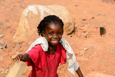 ELMINA, GHANA -JAN 18, 2017: Unidentified  Ghanaian little girl with braids in red dress walks on the sand in Elmina. Children of Ghana suffer of poverty due to the bad economyのeditorial素材