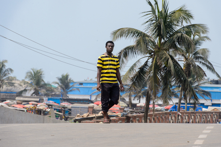 ELMINA, GHANA -JAN 18, 2017: Unidentified  Ghanaian man walks on the street with backpack in Elmina. People of Ghana suffer of poverty due to the bad economy.のeditorial素材