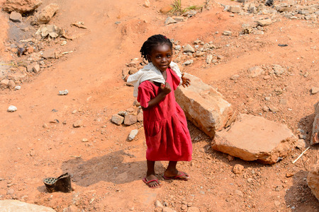 ELMINA, GHANA -JAN 18, 2017: Unidentified  Ghanaian little girl with braids in red dress walks on the sand in Elmina. Children of Ghana suffer of poverty due to the bad economyのeditorial素材