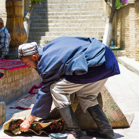 SAMARKAND, UZBEKISTAN - JUNE 10, 2011: Unidentified Uzbek carpet seller collects the carpets in Uzbekistan, Jun 10, 2011.  81% of people in Uzbekistan belong to Uzbek ethnic groupのeditorial素材