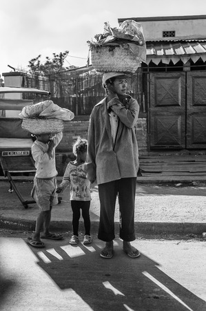 ANTANANARIVO, MADAGASCAR - JUNE 29, 2011: Unidentified Madagascar woman carries a huge bag on her head as her children do. People in Madagascar suffer of poverty due to the slow development of the countryのeditorial素材