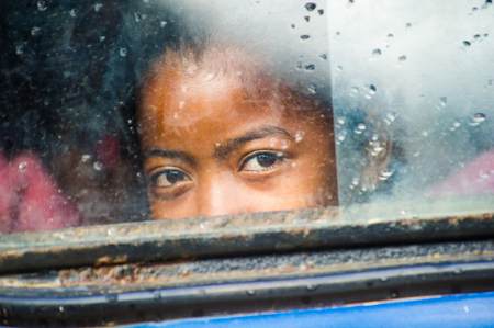 MADAGASCAR - JUNE 28, 2011: Unidentified Madagascar girl smiles for the camera through the school bus window in Madagascar, June 28, 2011. Children of Madagascar suffer of poverty due to the unstable situation.のeditorial素材