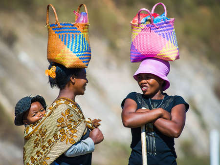 ANTANANARIVO, MADAGASCAR - JUNE 27, 2011: Unidentified Madagascar women walk and carry bags on their heads and a baby on a back. People in Madagascar suffer of poverty due to the slow development of the countryのeditorial素材