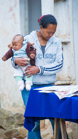 ANTANANARIVO, MADAGASCAR - JUNE 29, 2011: Unidentified Madagascar woman carries her baby and reads a newspaper. People in Madagascar suffer of poverty due to the slow development of the countryのeditorial素材