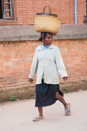 ANTANANARIVO, MADAGASCAR - JUNE 30, 2011: Unidentified Madagascarwoman carries a bag on the head. People in Madagascar suffer of poverty due to the slow development of the countryのeditorial素材