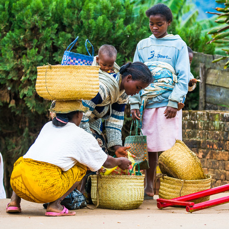 ANTANANARIVO, MADAGASCAR - JUNE 30, 2011: Unidentified Madagascar woman with her baby on the back buys something. People in Madagascar suffer of poverty due to the slow development of the countryのeditorial素材