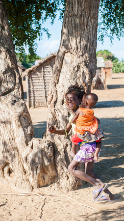 ANTANANARIVO, MADAGASCAR - JULY 3, 2011: Unidentified Madagascar girl runs holding her little brother. People in Madagascar suffer of poverty due to slow development of the countryのeditorial素材