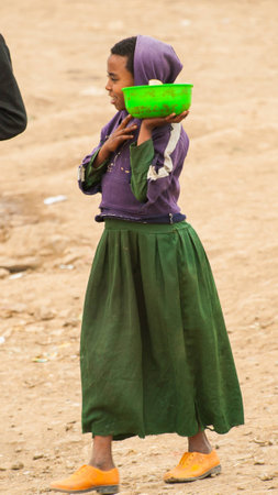 OMO, ETHIOPIA - SEPTEMBER 22, 2011: Unidentified Ethiopian girl carries a dish with food. People in Ethiopia suffer of poverty due to the unstable situationのeditorial素材