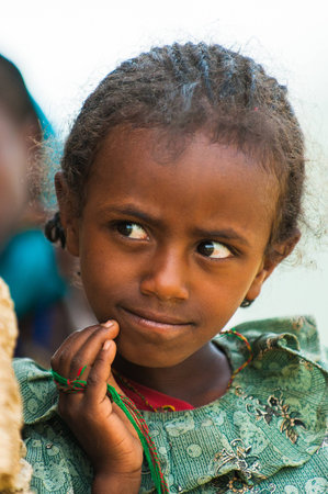AKSUM, ETHIOPIA - SEP 24, 2011: Unidentified Ethiopian cute little girl in green dress near the stone wall in Ethiopia, Sep.24, 2011. Children in Ethiopia suffer of poverty due to the unstable situationのeditorial素材