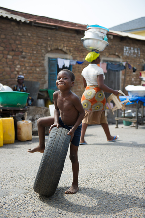 GHANA - MARCH 2, 2012: Unindentified Ghanaian boy plays with a car tire on the street in Ghana, on March 2nd, 2012. People in Ghana suffer from poverty due to the slow development of the countryのeditorial素材