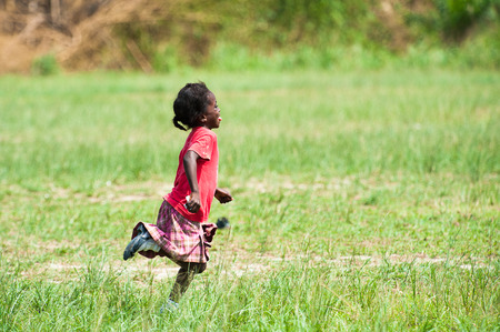 GHANA - MARCH 3, 2012: Unindentified Ghanaian girl in red clothes runs happily in the field in Ghana, on March 3rd, 2012. Children in Ghana suffer from poverty due to the unstable economical situationのeditorial素材
