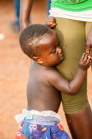 ACCRA, GHANA - MARCH 5, 2012: Unidentified Ghanaian boy near the legs of his mother in the street in Ghana. Children of Ghana suffer of poverty due to the unstable economic situationのeditorial素材