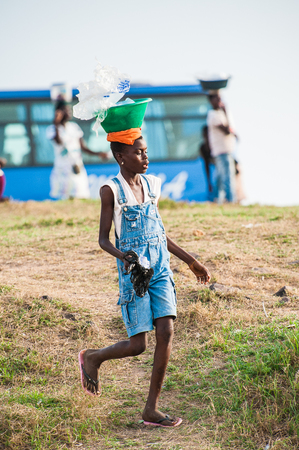 ACCRA, GHANA - MARCH 2, 2012: Unidentified Ghanaian girl carries a pelvis on her head in Ghana. People of Ghana suffer of poverty due to the unstable economic situationのeditorial素材