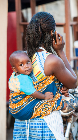 ACCRA, GHANA - MARCH 3, 2012: Unidentified Ghanaian woman carries her little baby on her back in Ghana. People of Ghana suffer of poverty due to the unstable economic situationのeditorial素材