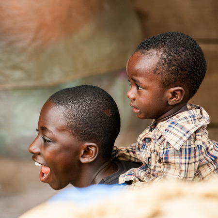ACCRA, GHANA - MARCH 4, 2012: Unidentified Ghanaian boy carries his brother on his back in the street in Ghana. Children of Ghana suffer of poverty due to the unstable economic situationのeditorial素材