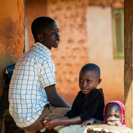 ACCRA, GHANA - MARCH 5, 2012: Unidentified Ghanaian man and his children near the housein the street in Ghana. People of Ghana suffer of poverty due to the unstable economic situationのeditorial素材