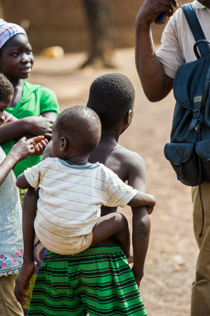 ACCRA, GHANA - MARCH 6, 2012: Unidentified Ghanaian boy carries his little brother on his back in the street in Ghana. Children of Ghana suffer of poverty due to the unstable economic situationのeditorial素材