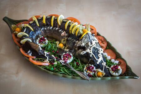 Image of a sturgeon decorated with lemon and tomatoes on a green plateの写真素材