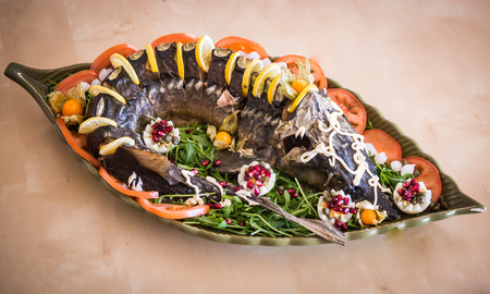 Image of a sturgeon decorated with lemon and tomatoes on a green plateの写真素材