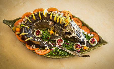 Image of a sturgeon decorated with lemon and tomatoes on a green plateの写真素材