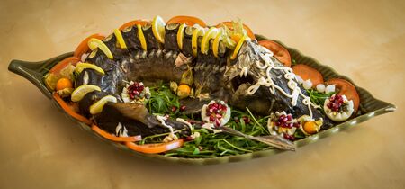 Image of a sturgeon decorated with lemon and tomatoes on a green plateの写真素材