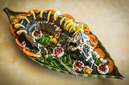 Image of a sturgeon decorated with lemon and tomatoes on a green plateの写真素材