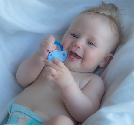 Laughing baby with blue eyes playing with pacifierの写真素材