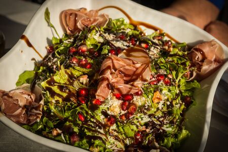 Image of green salad with ham, pomegranate, cheese and special sauceの写真素材