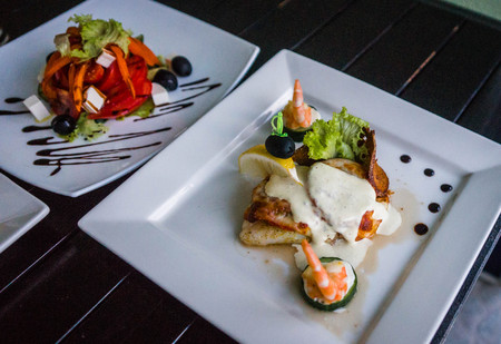 Image of decorated fish with seasonings, sauce and cheese on a white square plate. selective focus
