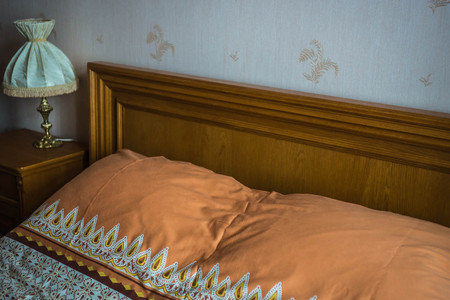 Image of beautifull linens, pillows and blankets on brown wooden bed and bed-side lampの写真素材