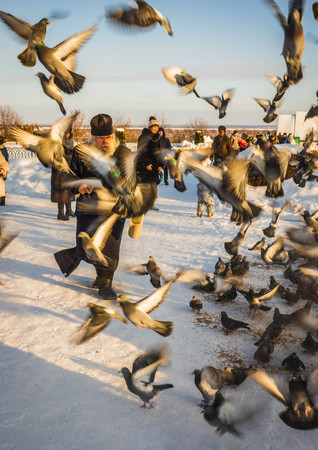 Murom, Russia - January 07, 2019: Orthodox priest feeding pigeons in the Spaso-Preobrazhensky monastery in Murom, Russiaのeditorial素材