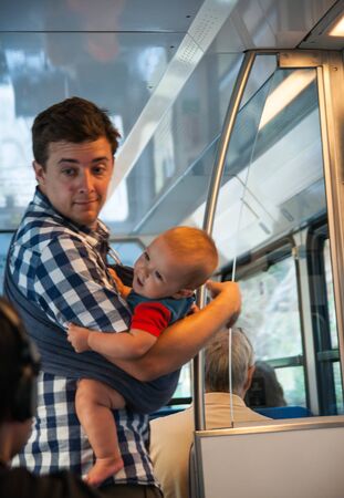 Diakopto-Kalavrita, Greece - August 04, 2012, Young man and his little baby in sling  in sunset lighting traveling in train car in Diakopto-Kalavrita train, Greeceのeditorial素材