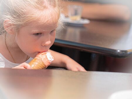 Image of little blonde girl eating white and pink ice cream in a waffle cone