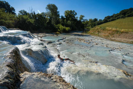 Saturnia, Italy - June 24, 2020, Two asian children taking bath in natural spa with waterfalls and hot springs at thermal baths in Saturnia, Tuscany in Italyのeditorial素材