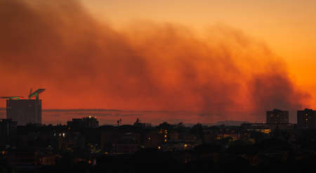 Image of smoke from a fire over a night city on a sunset sky in Rome, Italy