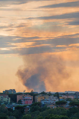 Image of smoke from a fire over a city on early sunset sky in Rome, Italy