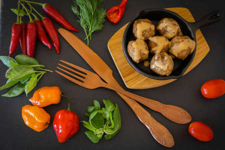 Image of meatballs with French sauce in a small skillet on a wooden stand with old cutlery and...