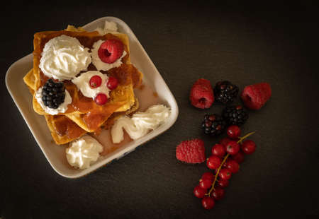 Image of waffles with whipped cream, raspberries, blackberries and red curd on a dark backgroundの写真素材