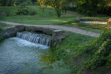 Image of small waterfall on a green river in a park in Italyの写真素材