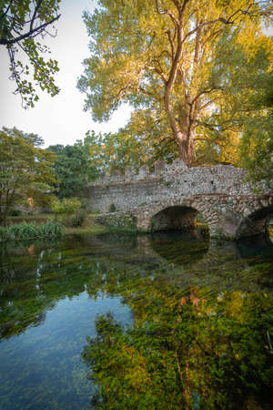 Image of stone bridge with arches and reflection in the water in the Nymph Gardens in the province...