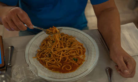 Image of roman spaghetti with tomato sauce, bacon and male hands with a forkの写真素材