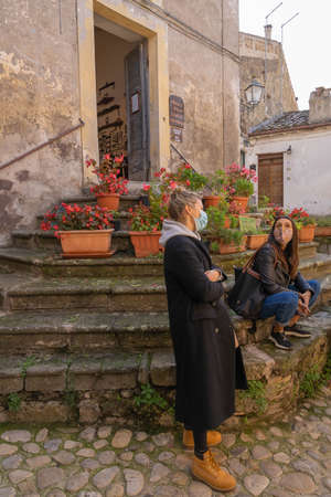Calcata Vecchia, Italy - October 20, 2020, Masked people on stone steps with a lot of flowers of Calcata Vecchia, Italy. Second wave of coronavirus (covid19), keeping social distanceのeditorial素材