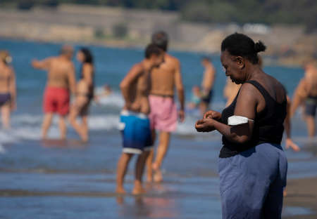 Marina di San Nikola, Italy - September 05, 2021, African woman walking among a crowd of europeans on the beach in Marina San Nicola in Italyのeditorial素材