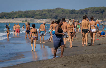 Marina di San Nikola, Italy - September 05, 2021, African woman walking among a crowd of europeans on the beach in Marina San Nicola in Italyのeditorial素材