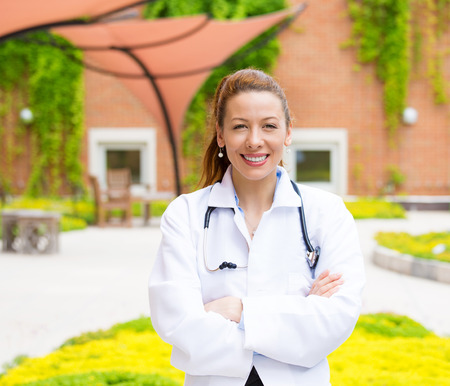 Closeup portrait, young smiling confident female doctor, arms crossed, healthcare professional, isolated outside hospital の写真素材