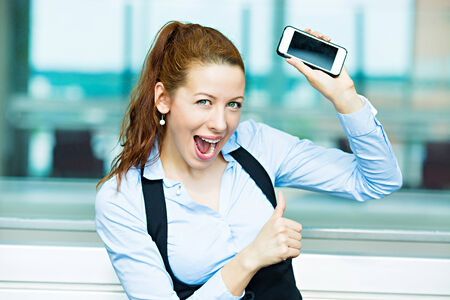 Closeup portrait happy, excited, young, attractive business woman, company employee showing, holding her smart phone, giving thumbs upの写真素材